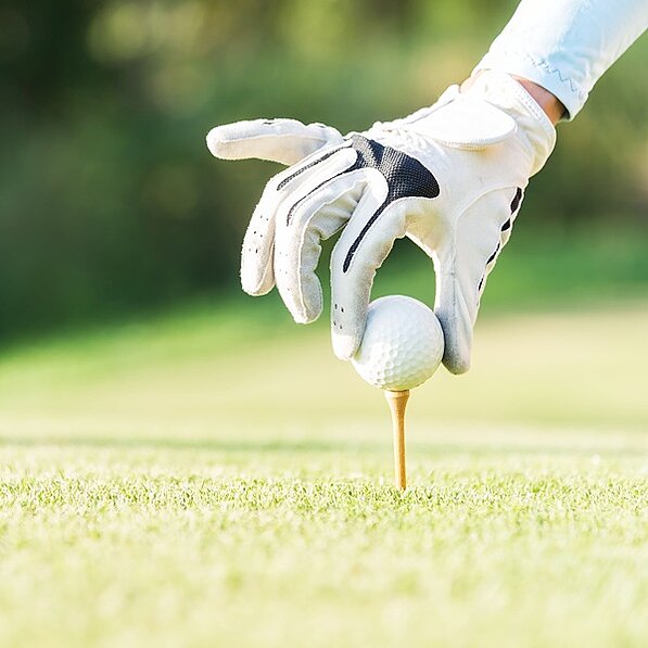Hand in Handschuh teet einen Golfball auf dem Green auf